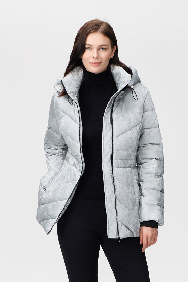 A woman modeling a light gray quilted puffer jacket with a black turtleneck, black leggings, and black boots, standing against a plain light gray studio background.