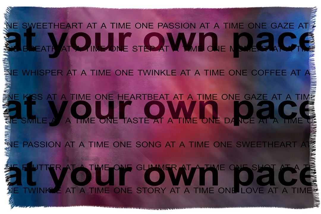 A square throw blanket with fringed edges featuring a colorful gradient background of pink, purple, and blue, overlaid with the text 'at your own pace' repeated in black.