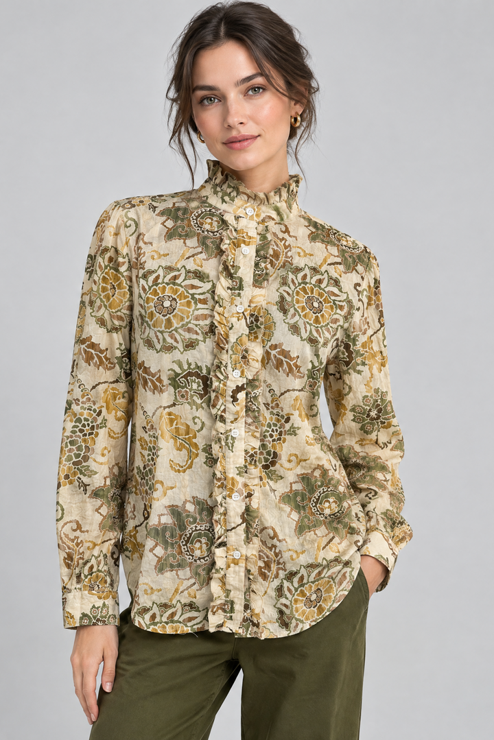 A woman modeling a long-sleeve high-neck button-up blouse with an intricate floral and paisley pattern in olive green, mustard yellow, and beige, paired with olive green pants, against a solid light gray background.