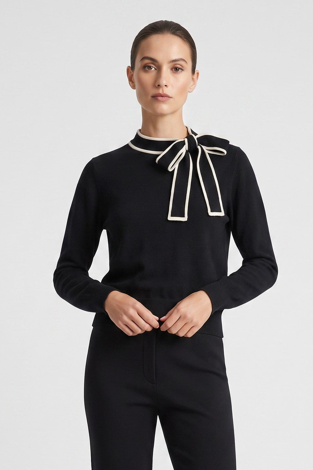 Just Perfect Collection Online black knit sweater featuring a white-trimmed bow tie neck detail worn by a model