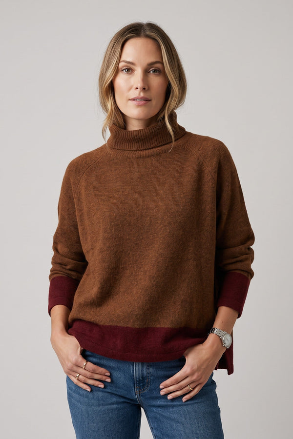Model wearing a Just Perfect Collection Online bronze dolman sleeve turtleneck sweater with a dark red hem.